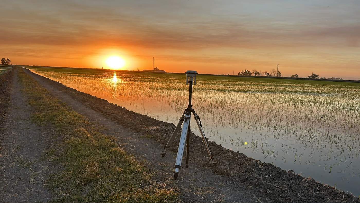 Base GNSS/RTK de DroneSevilla junto a un cultivo de arroz en Sevilla al atardecer, para el posicionamiento de precisión